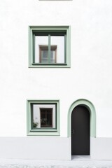 Exterior view of a minimalist building featuring green-framed windows and a distinctive arched door designed for modern urban architecture in a serene neighborhood