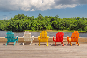 A row of brightly colored adirondack chairs along waterfront in summer.