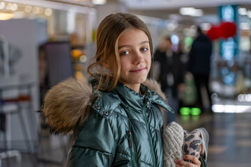 Winter Portrait: A smiling young girl in a puffy coat with fur trim and mittens indoors during the...