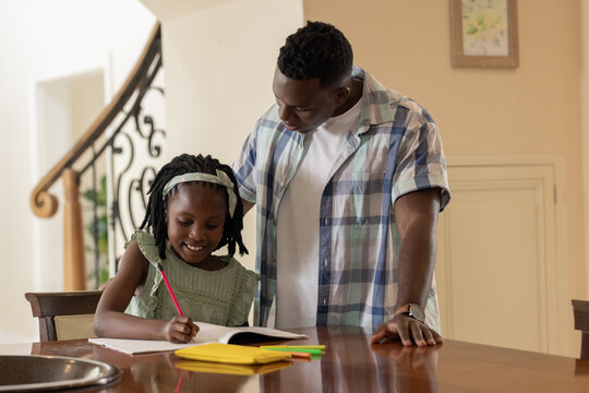 African American father helping daughter with homework at home, both smiling warmly