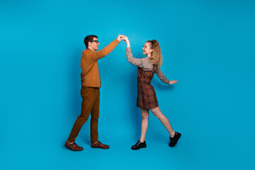 Fototapeta premium Young couple joyfully dancing against bright blue background, showcasing retro-style clothing and lively expressions