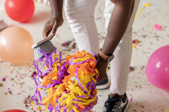 At party, Sweeping colorful confetti and balloons, African American person tidying after party celeb