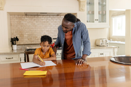 Father helping son with homework at kitchen table, focusing on learning