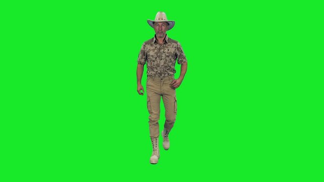 Handsome strong mid adult man in camouflage uniform and cowboy hat walking on green chroma key bacreckground, Front view, 4k pre-keyed footage