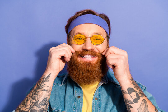 Stylish bearded man wearing a headband and yellow sunglasses smiling confidently, showcasing his trendy casual fashion