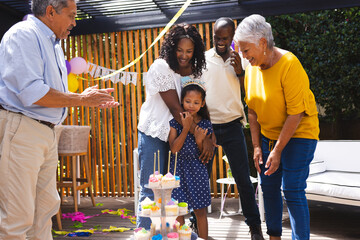 At party, Happy family celebrating birthday in garden, smiling and clapping around cake with candles