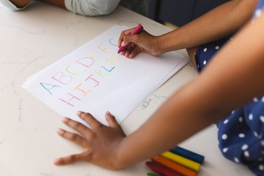 Child practicing alphabet writing with colorful crayons on paper at home