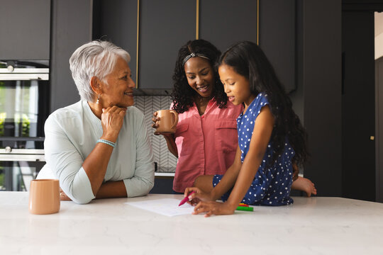 Three happy generations of women enjoying time at kitchen table with coffee, at home