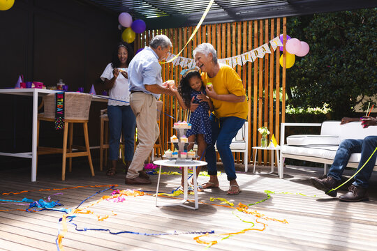 At party, celebrating birthday in garden, happy family dancing with child, grandparents smiling