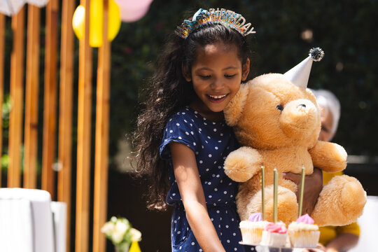 At party, Smiling girl holding teddy bear at birthday party with cupcakes and candles