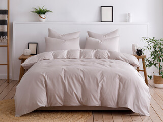 Modern bedroom with white walls, wooden floors, and handmade furniture. Double bed with four pillows is neatly made up with a fluffy duvet in a beige duvet cover. Front view photo. Suitable for mockup