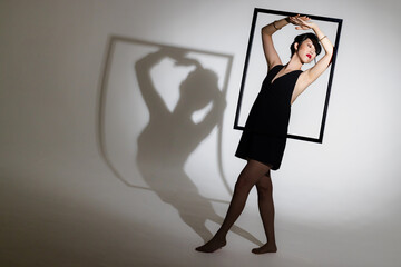 Model posing creatively with picture frame, casting dramatic shadow on wall, copy space