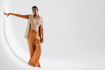 Model posing in stylish beige outfit, leaning gracefully against white wall, copy space