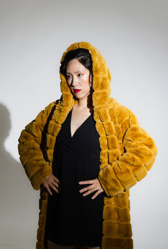Confident asian woman in luxurious fur coat posing in modern fashion studio