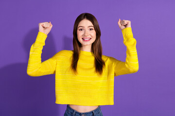 Cheerful young woman wearing a bright yellow sweater smiling and raising her arms in celebration...