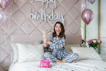 Fototapeta premium Young woman celebrating birthday opening firecracker on bed