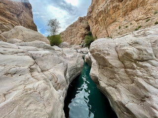 Stunning Turquoise Water Flows Through Rocky Canyon in Wadi Bani Khalid, Oman - Scenic Landscape View of Natural Wonder in Middle East (177 characters)