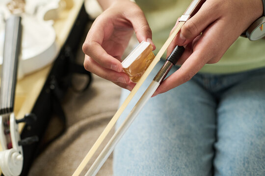 Detailed view of hands applying rosin on violin bow. Instrument and musician's focused preparation for a performance or practice session captured in the moment