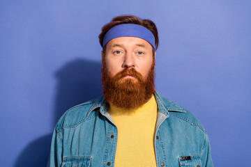 Portrait of a stylish man with a red beard wearing a blue headband and casual denim jacket against a vibrant purple background