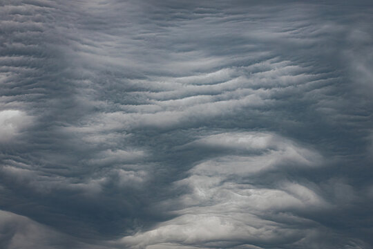 A dramatic display of undulatus asperatus clouds forms wavy, textured layers across the sky, creating a surreal and turbulent atmosphere. Includes copy space.