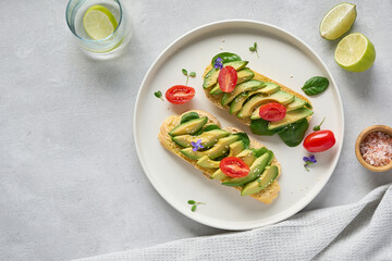 Toasts of sourdought bread with avocado slices, red cherry tomatoes and microgreen. Top view with grey background, copy space.      