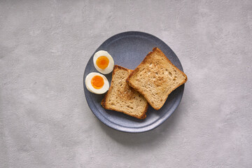 A boiled egg with vibrant yolk and toast for breakfast served on a blue ceramic plate. Creative simple breakfast concept against grey background. Vegetarian breakfast    