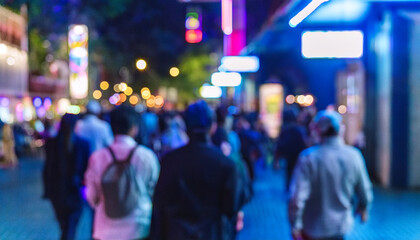 Personas variadas caminando con desenfoque de movimiento por por la noche una calle de ciudad  iluminada con ambiente cálido