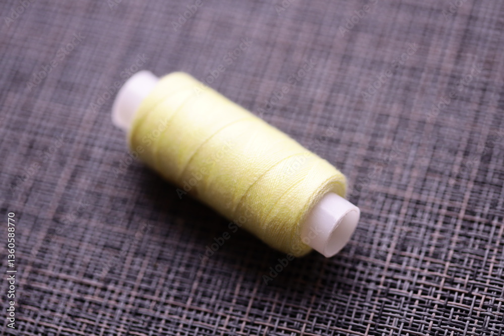 Poster a single spool of yellow thread sits on a table, ready for use.