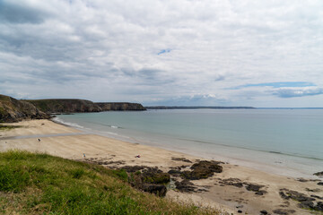 Quelques personnes profitent de la plage du Veryac’h par une journée d’été, sous un ciel très nuageux, tandis que la mer paisible effleure le rivage.