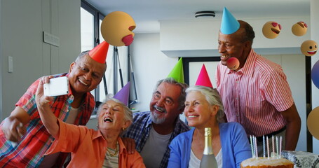 Elderly friends wearing party hats taking selfie during birthday celebration at home