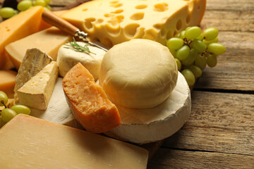 Different types of cheese and grapes on wooden table, closeup