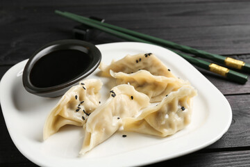 Delicious gyoza dumplings with sesame seeds served on black wooden table, closeup