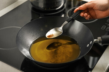 Woman holding spoon over frying pan with used cooking oil at stove, closeup