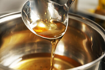Pouring used cooking oil from ladle into saucepan, closeup