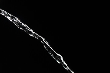 Crystal clear stream of water flowing on isolated black background, closeup. Transparent pouring stream of clean water cascading against a dark backdrop. Concept of drinking pure water