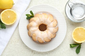 Delicious lemon cake with glaze, mint and citrus fruits on light textured table, flat lay