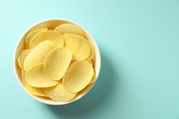 Tasty potato chips in bowl on light blue background, top view. Space for text