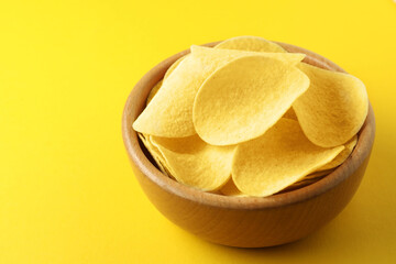 Tasty potato chips in bowl on yellow background, closeup. Space for text