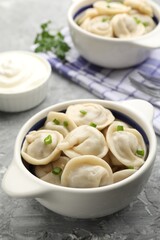 Delicious dumplings (pelmeni) with green onion in bowl on grey table, closeup