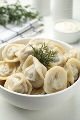 Tasty dumplings and dill in bowl on white table, closeup