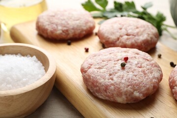 Many uncooked patties and spices on wooden table, closeup