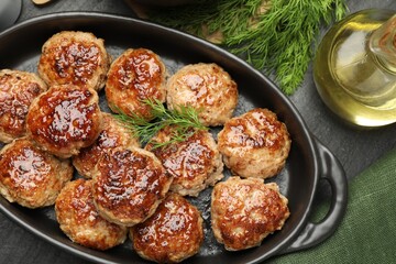 Delicious patties in baking dish, dill and oil on black table, flat lay