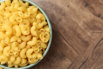 Raw horns pasta in bowl on wooden table, top view. Space for text
