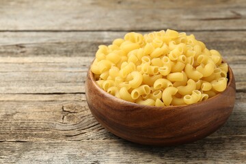 Raw horns pasta in bowl on wooden table, closeup