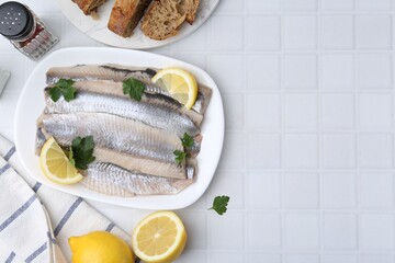 Marinated herring fillets with lemon, parsley and spices on white tiled table, flat lay. Space for...