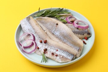 Marinated herring fillets with onion rings, rosemary and peppercorns on yellow background, closeup