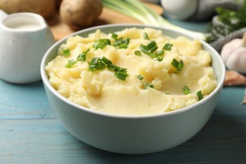 Delicious mashed potato with green onions in bowl on light blue wooden table, closeup