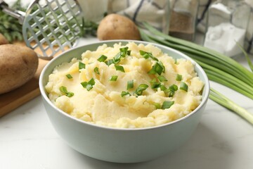 Delicious mashed potato with green onions in bowl on white marble table, closeup