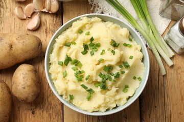 Delicious mashed potato with green onions served on wooden table, flat lay