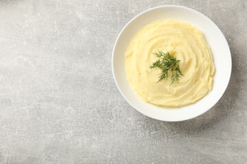 Tasty mashed potato with dill in bowl on grey textured table, top view. Space for text